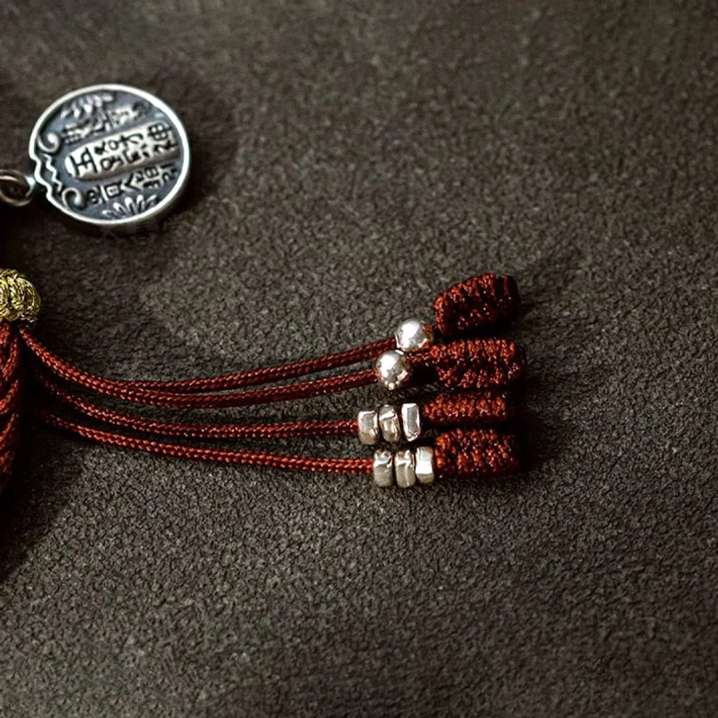 Close up of tassel and silver bead details on wealth luck red string bracelet