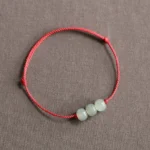 Three jade beads red string bracelet flat lay on gray background - authentic feng shui prosperity bracelet