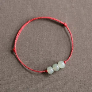 Three jade beads red string bracelet flat lay on gray background - authentic feng shui prosperity bracelet