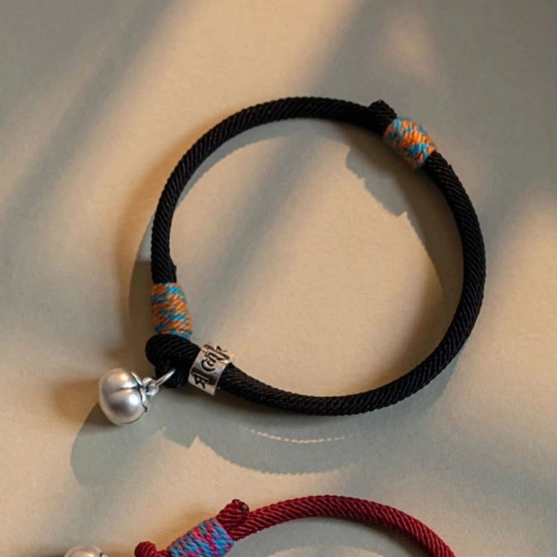 Black Tibetan braided luck bracelet with silver bell and engraved mantra bead close view