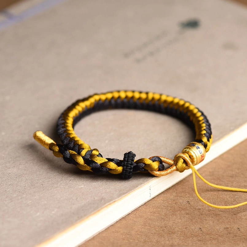 Tibetan mantra bracelet with long adjustment cords and engraved sacred metal bead on paper background
