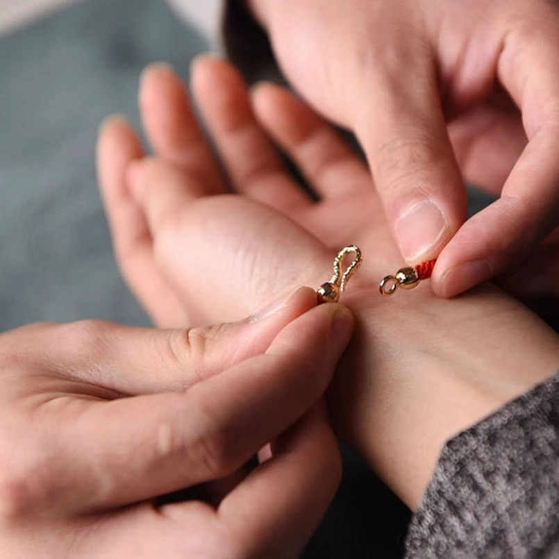 Hands demonstrating how to fasten and adjust gold toggle clasp on red string tibetan bracelet, wearing demo