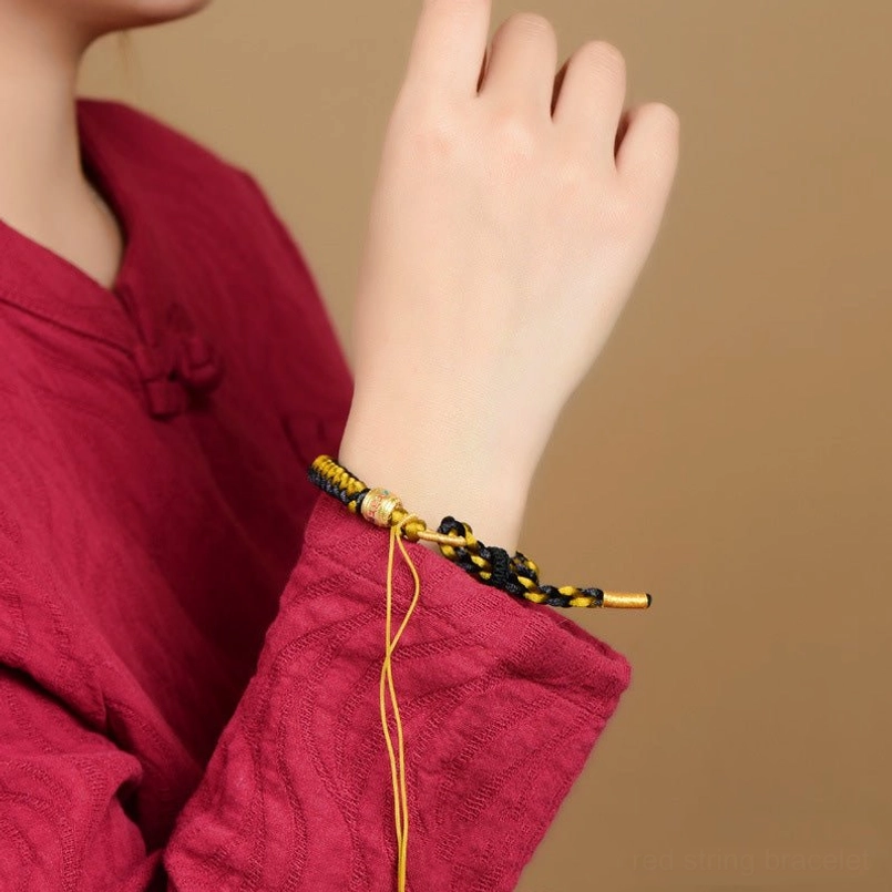 Tibetan bracelet being worn on wrist with red traditional clothing background showing adjustable cords