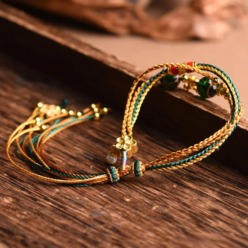 Two handcrafted tibetan healing bracelets with gold flower charms displayed on wooden tray