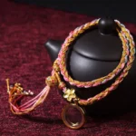 Tibetan lucky braided colorful string bracelet double wrap with copper flower charm and metal pendant on burgundy fabric background