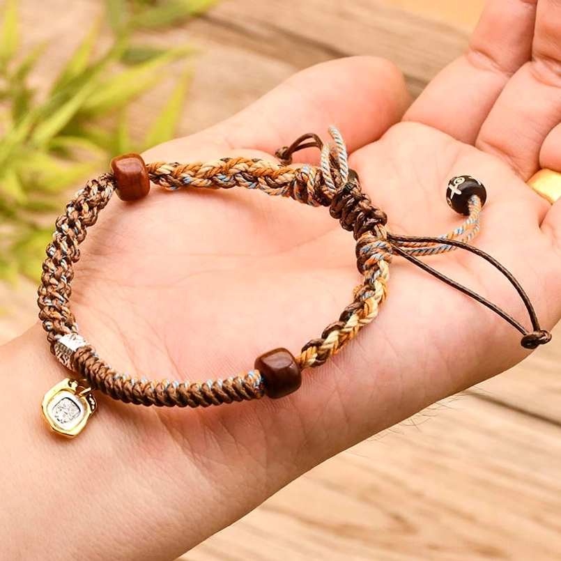 Tibetan light brown braided wealth protection bracelet held in palm with green foliage background