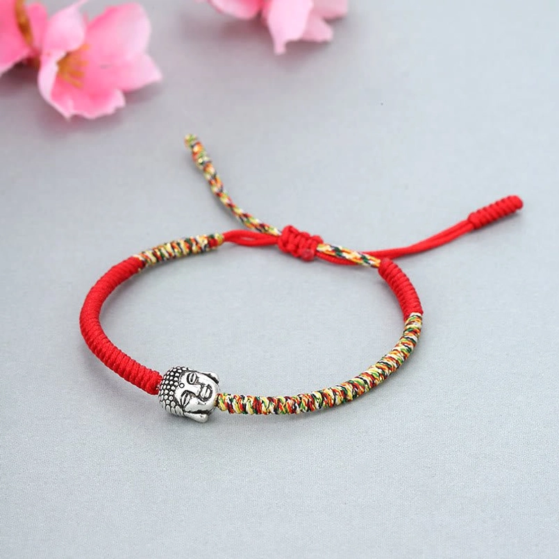Tibetan Buddhist knot protection red string bracelet on light gray background with pink flowers