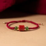 Tibetan cinnabar om mani padme hum red string bracelet with jade beads, top-down flat lay view