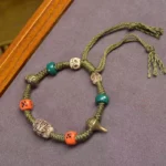 Tibetan dragon dice handmade green rope bracelet flat lay on gray fabric