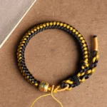 Tibetan black gold dragon scale Om Mani Padme Hum bracelet overhead view with engraved metal bead on brown paper