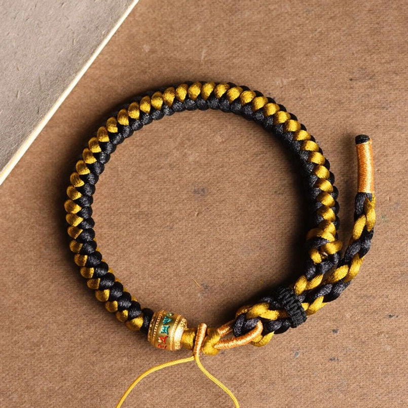 Tibetan black gold dragon scale Om Mani Padme Hum bracelet overhead view with engraved metal bead on brown paper