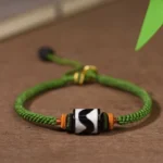 Handcrafted Tibetan Dzi bead green rope protection bracelet flat lay on wooden surface