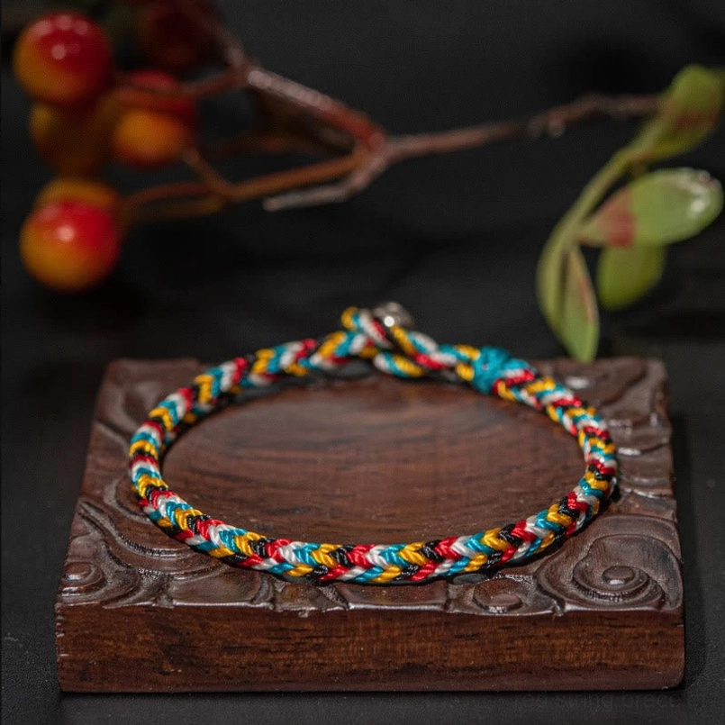 Tibetan five color thread red string bracelet top view on carved wooden coaster