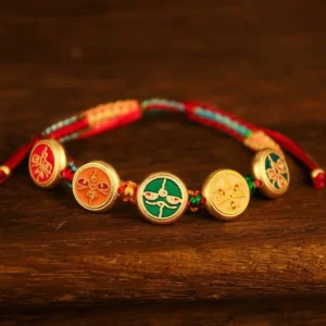 Tibetan Five Gods of Wealth braided luck bracelet flat lay with colorful rope and gold enamel charms on dark wood