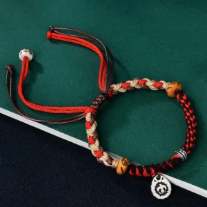 Red Tibetan Garuda hand-woven bracelet with wooden beads and silver pendant on green fabric