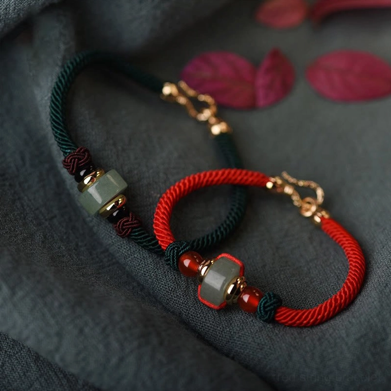 Couple's Tibetan Red String and Green Aventurine luck braided bracelets with jade beads and gold clasps, flat lay on fabric