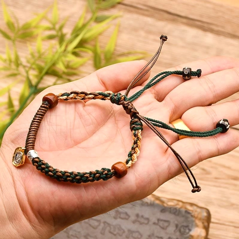 Tibetan green braided wealth protection bracelet held in palm with green foliage background