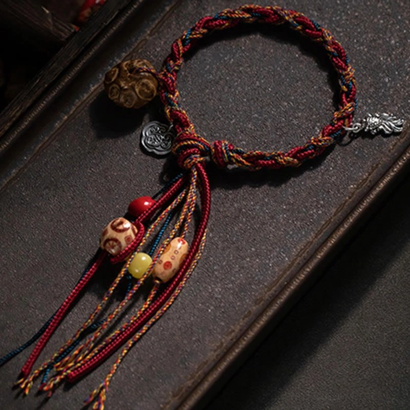 Overhead flat lay of handmade beaded woven bracelet with red rope and silver charms on wooden tray