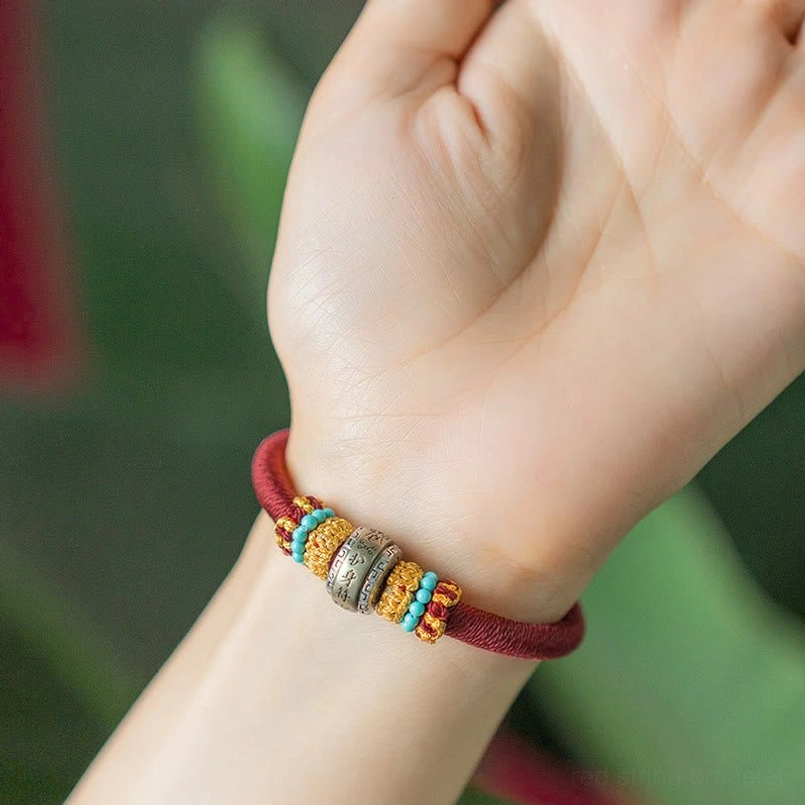 Red Tibetan protection bracelet worn on wrist with engraved metal charm close-up view