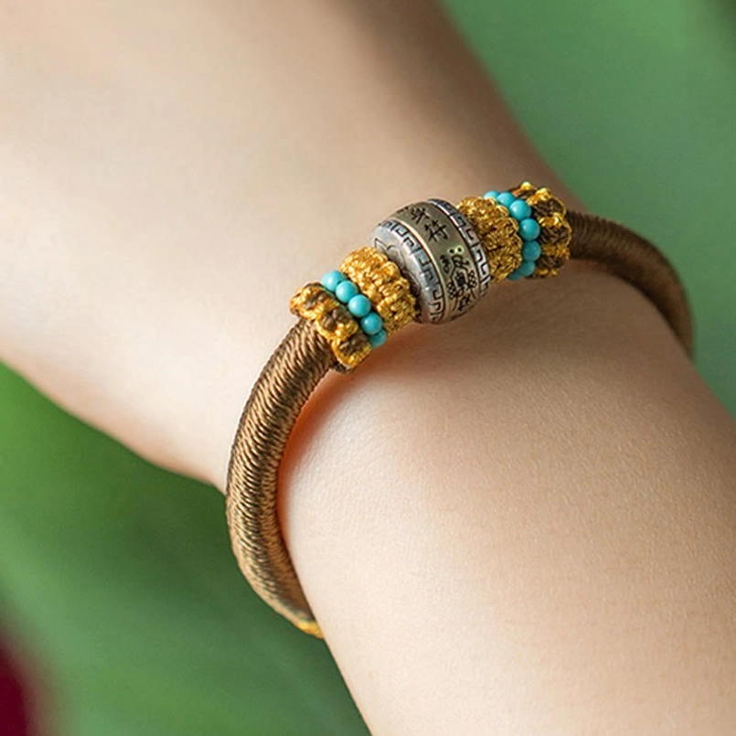 Brown handmade Tibetan protection bracelet on wrist with engraved metal amulet pendant