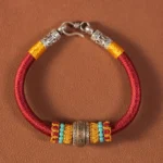 Red woven Tibetan King Kong Knot protection bracelet with silver metal charm on brown studio background