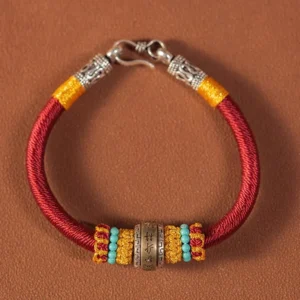 Red woven Tibetan King Kong Knot protection bracelet with silver metal charm on brown studio background