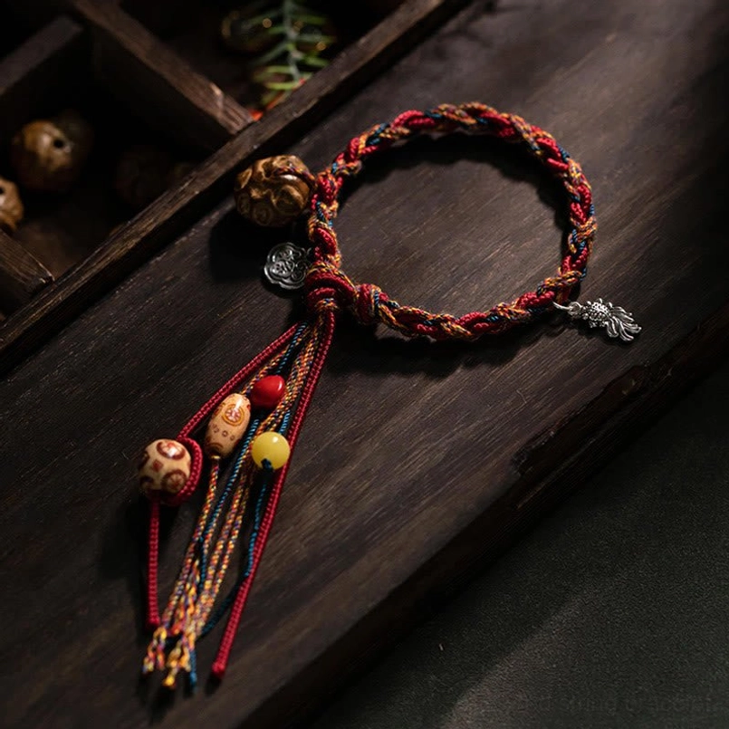 Tibetan koi fish red string bracelet with 925 sterling silver charms and beads displayed on dark wooden tray