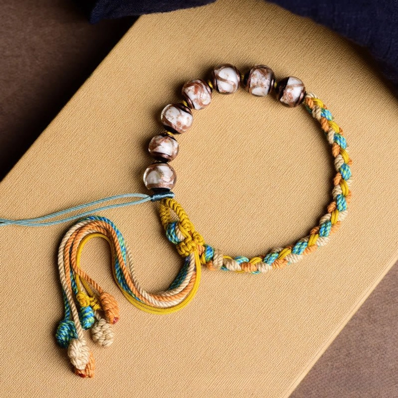 Flat lay Tibetan Liuli glass bracelet with yellow and blue braided cord and decorative tail