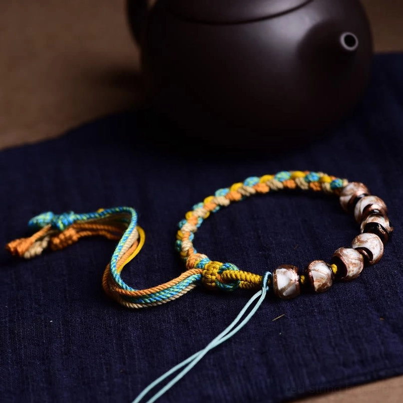 Side angle Tibetan Liuli glass bracelet with yellow-blue woven rope on dark surface