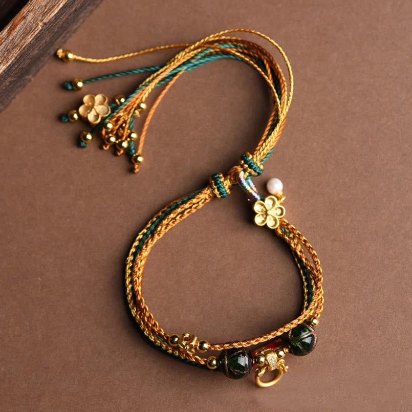 Handmade tibetan healing bracelet with four-leaf gold charm and white pearl pendant on brown background