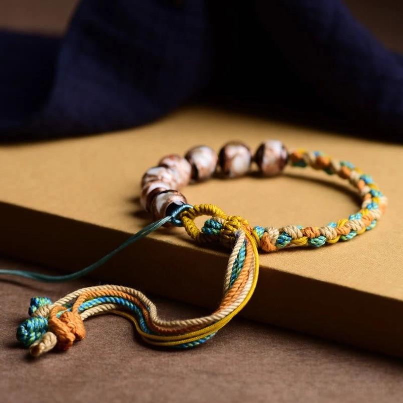 Tibetan Liuli glass bracelet with multi-color marbled beads and tassel pendant on wooden surface