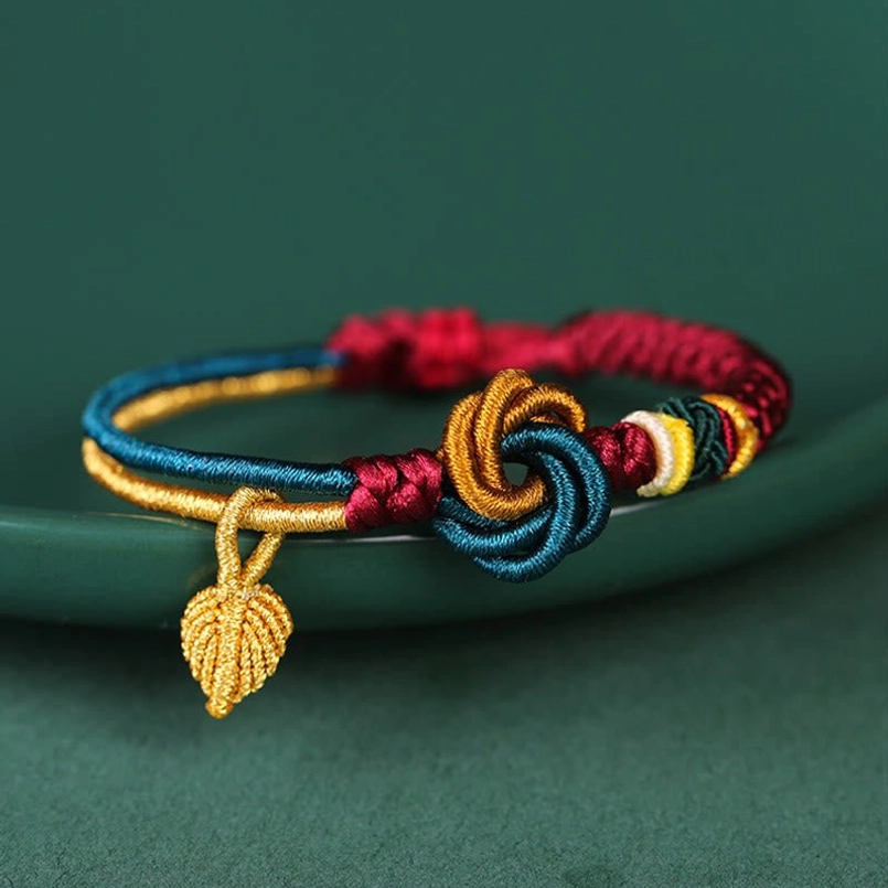 Red and gold Tibetan luck bracelet with flower knot design and leaf charm flat lay view