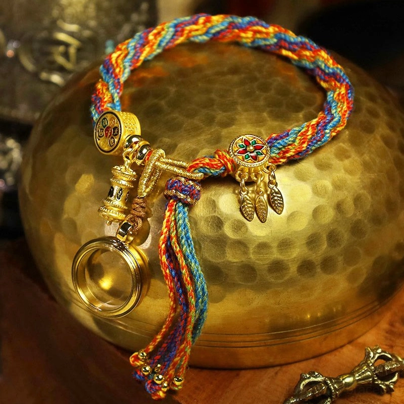 Tibetan red string bracelet with enamel flower charm resting on hammered brass vessel