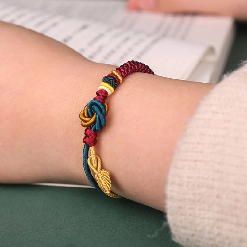Multi-color woven luck bracelet on wrist with golden leaf pendant and sweater sleeve visible