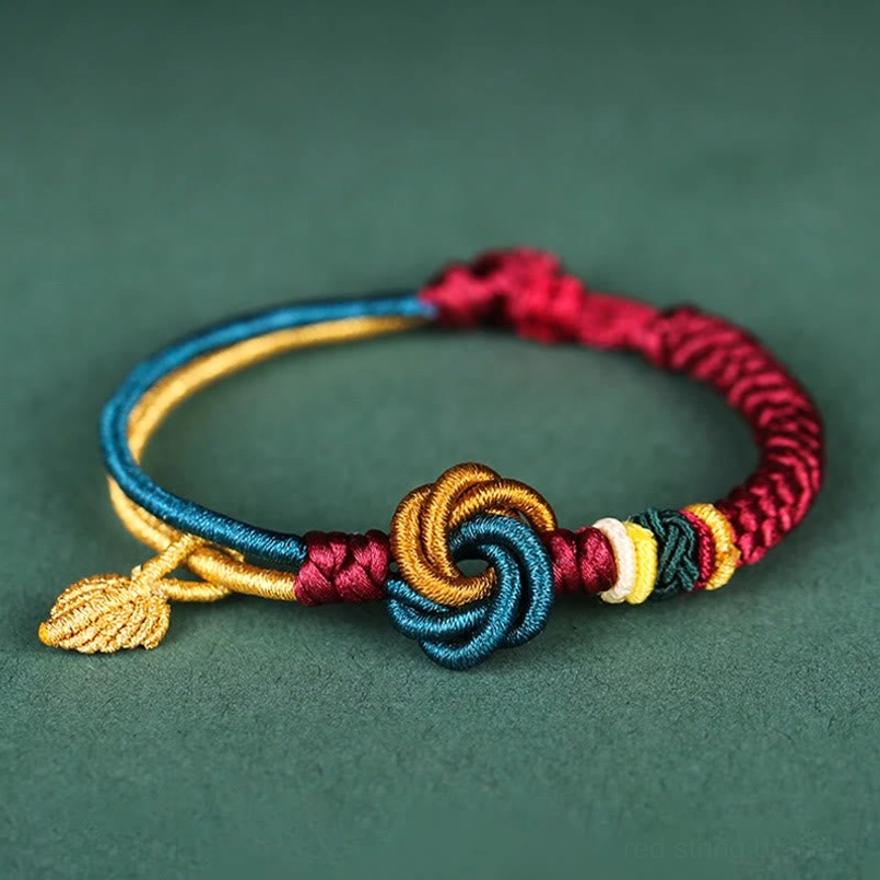 Tibetan mandala knot leaf bracelet handmade flat lay with golden charm on dark green background