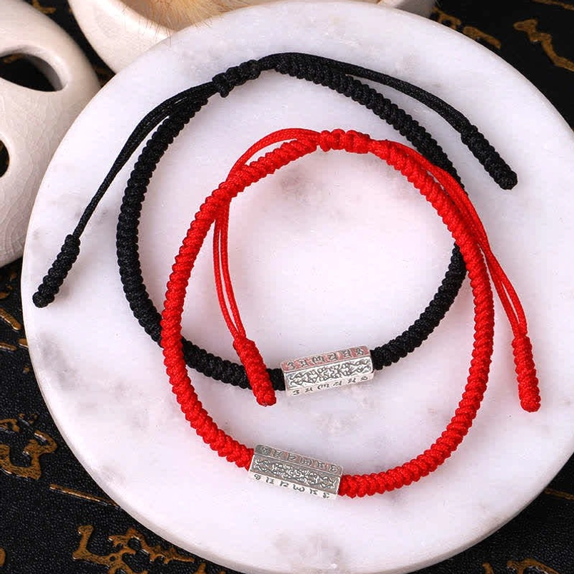 Red and black Om Mani Padme Hum luck bracelets with adjustable knots on marble background