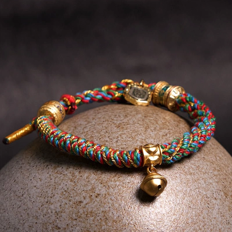 Om Mani Padme Hum red string bracelet with brass bell pendant - overhead angled view