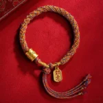 Tibetan Om Mani Padme Hum Ruyi multicolor braided bracelet flat lay with gold charms on red fabric