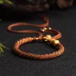 Tibetan handmade red braided prayer wheel bracelet with gold metal beads and tassel detail on dark background