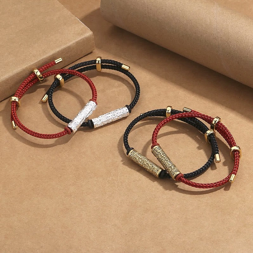 Tibetan braided lucky bracelets with engraved copper and silver metal tube accents on craft background
