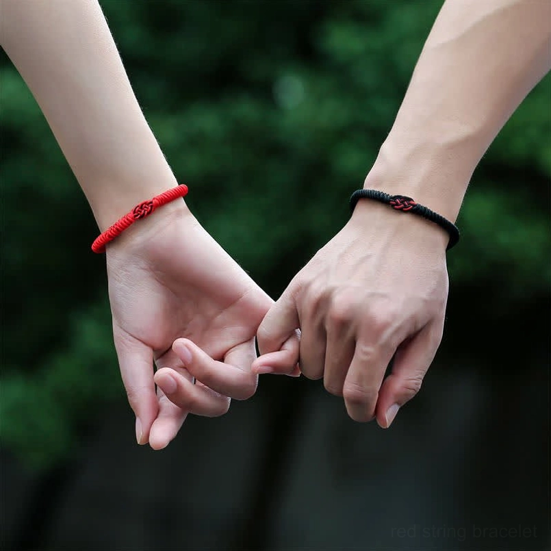Red and black Tibetan protection bracelets displayed on two hands outdoors with nature background