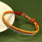 Handcrafted triple wrap colorful red string bracelet with chakra colors displayed on white ceramic plate with green background
