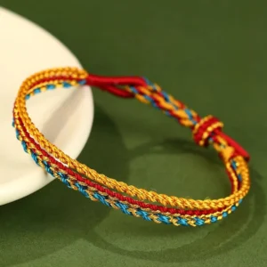 Handcrafted triple wrap colorful red string bracelet with chakra colors displayed on white ceramic plate with green background