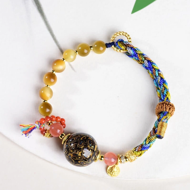 Tibetan lacquer tiger eye red string bracelet with golden small pendant top view on light desk