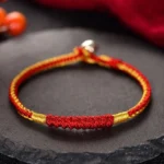 Tibetan handmade red braided protection bracelet with gold twisted cord and silver clasp on stone tray