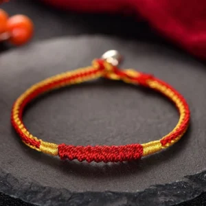 Tibetan handmade red braided protection bracelet with gold twisted cord and silver clasp on stone tray