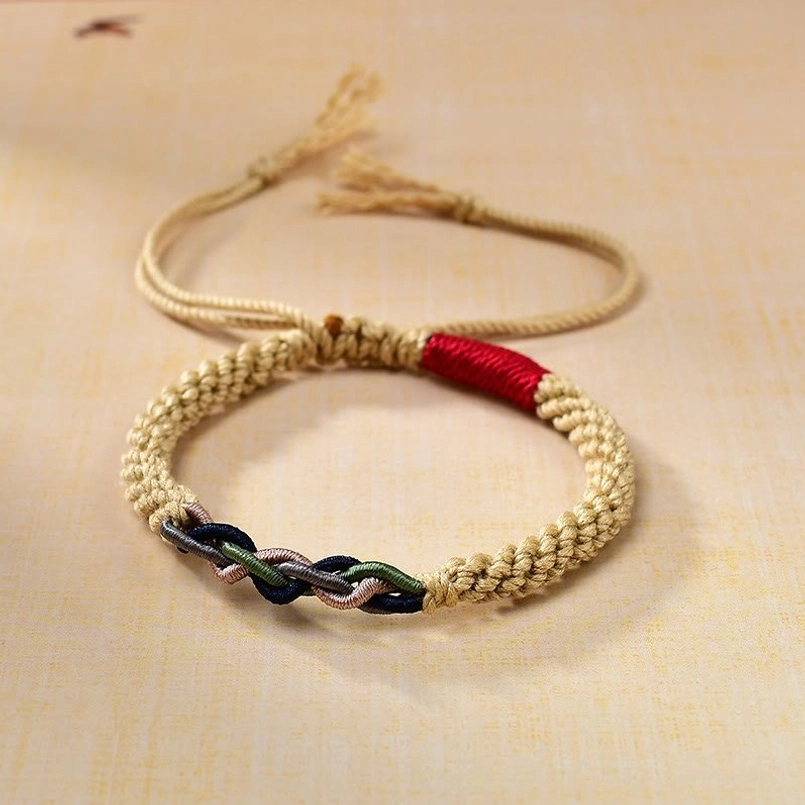 Tibetan hand-woven red string luck bracelet with beige cotton rope and red accent, featuring dual-color twisted knot and tassel tails on yellow background