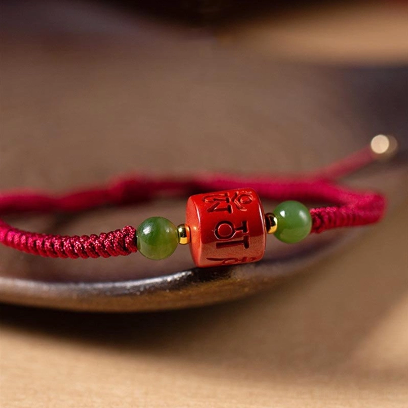 Macro close-up of Tibetan red string bracelet showing engraved mantra bead and jade beads