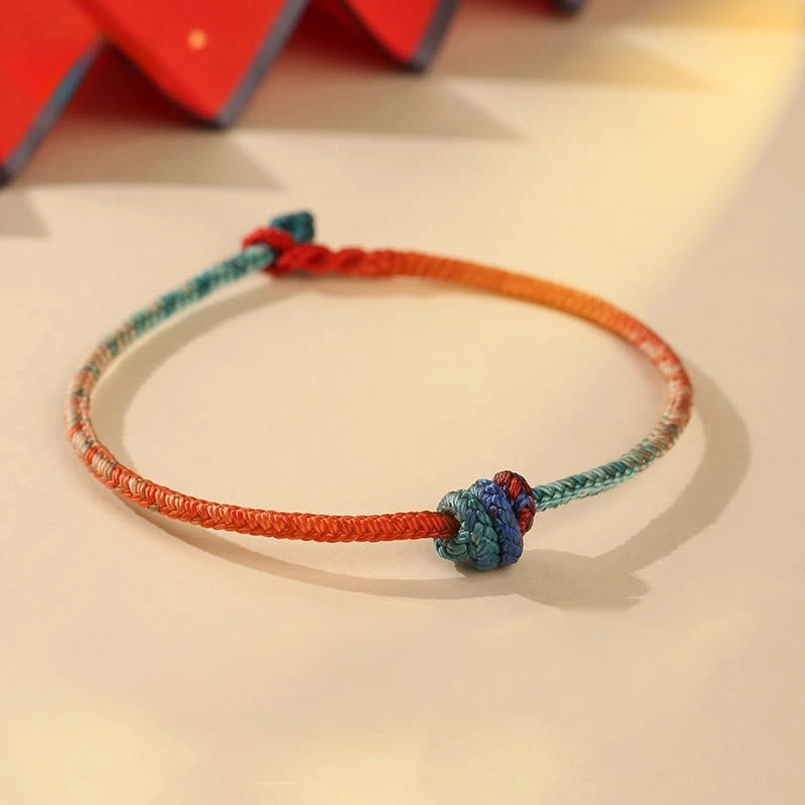 Hand-woven Tibetan red string bracelet with gradient teal color and decorative knots on beige background