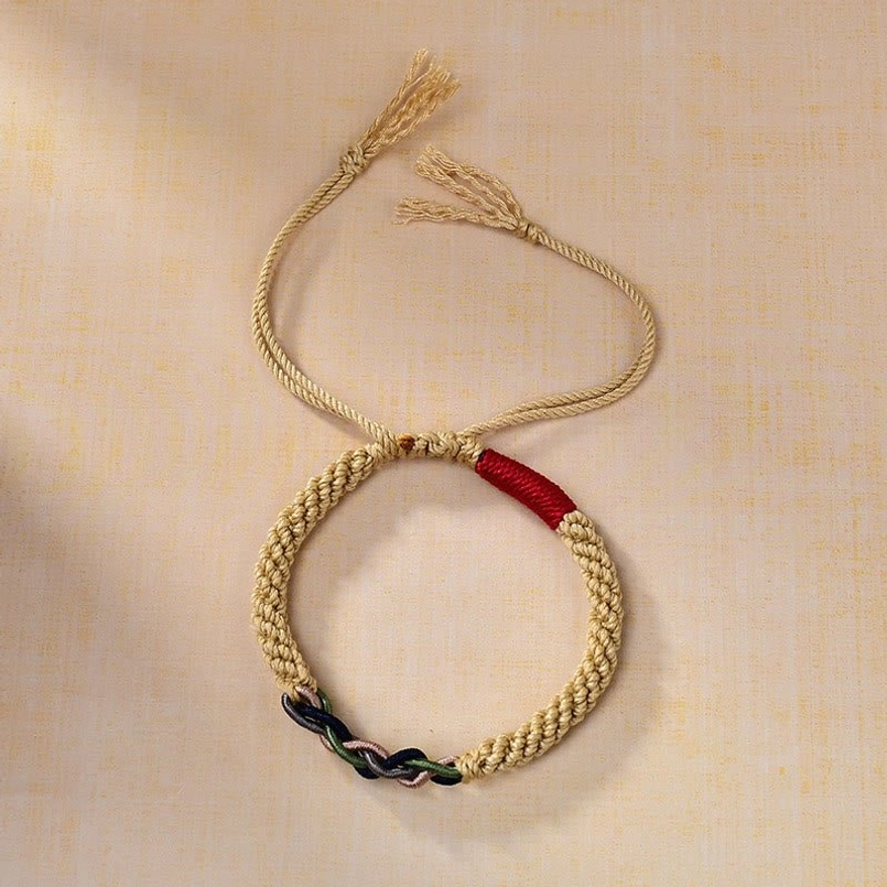 Oblique top-down shot of Tibetan hand-woven red string bracelet displaying craftsmanship with red upper accent and dual-color knotwork